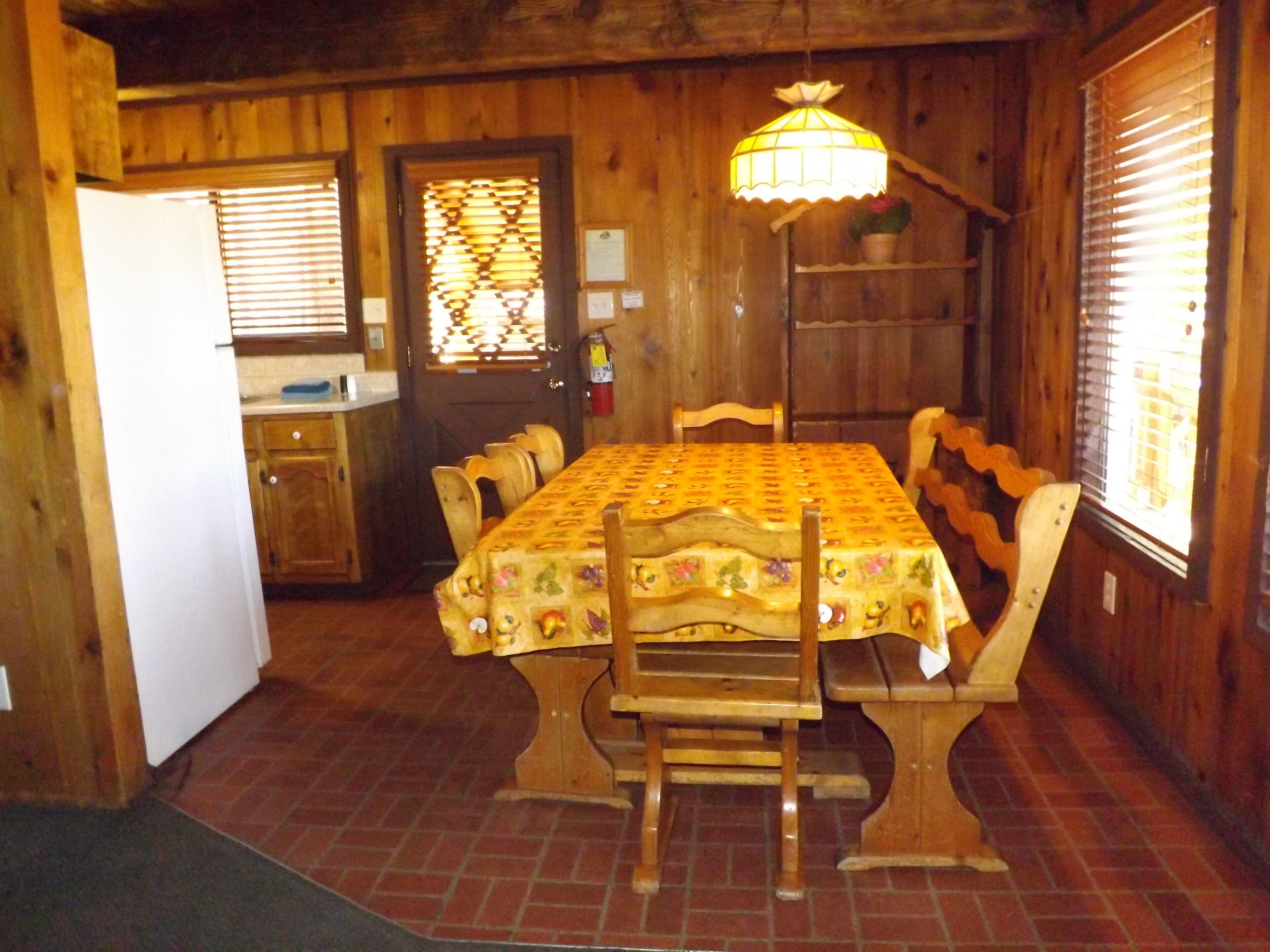 A wooden dining room with a table covered in a floral tablecloth, surrounded by wooden chairs.