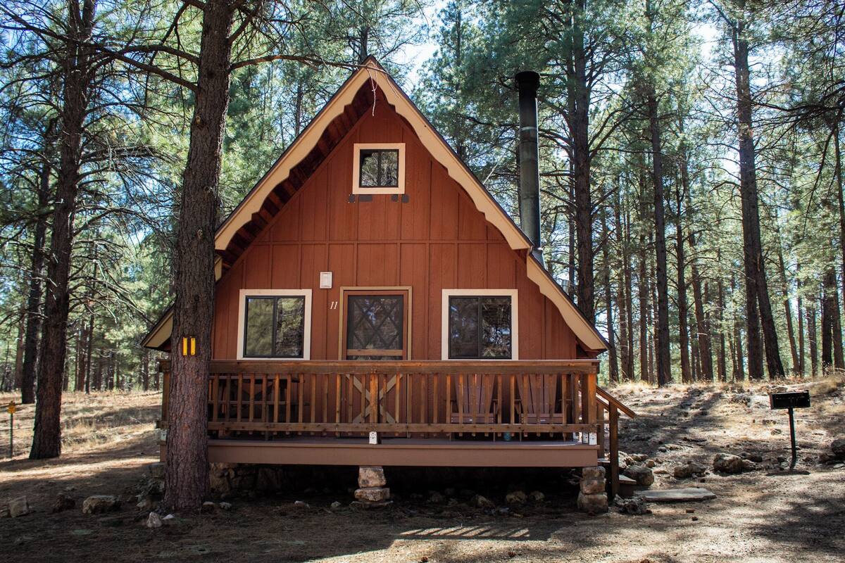 A wooden cabin with a balcony, surrounded by tall pine trees.