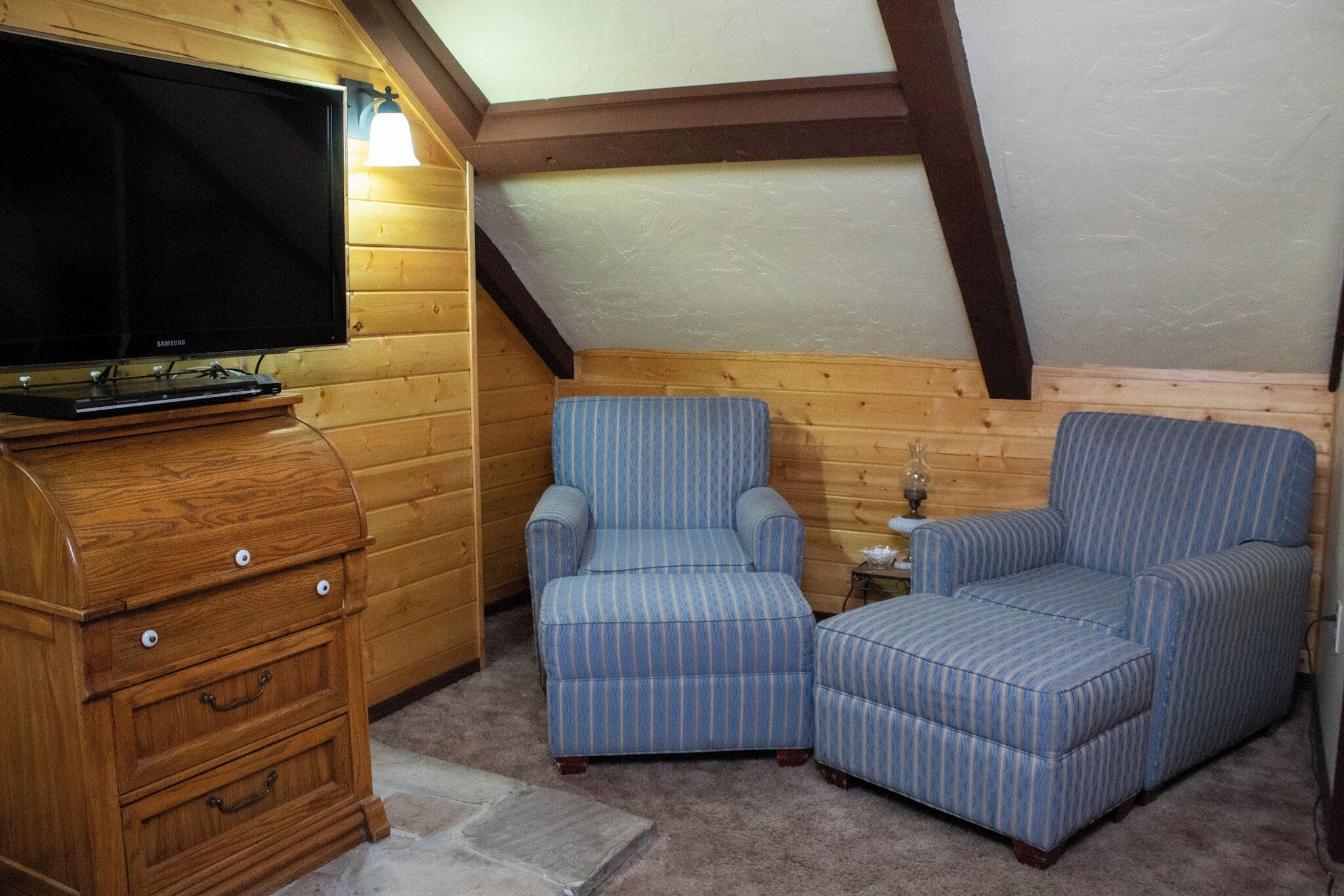A cozy room with a television on a wooden cabinet, two striped armchairs, and a small table with a lamp.