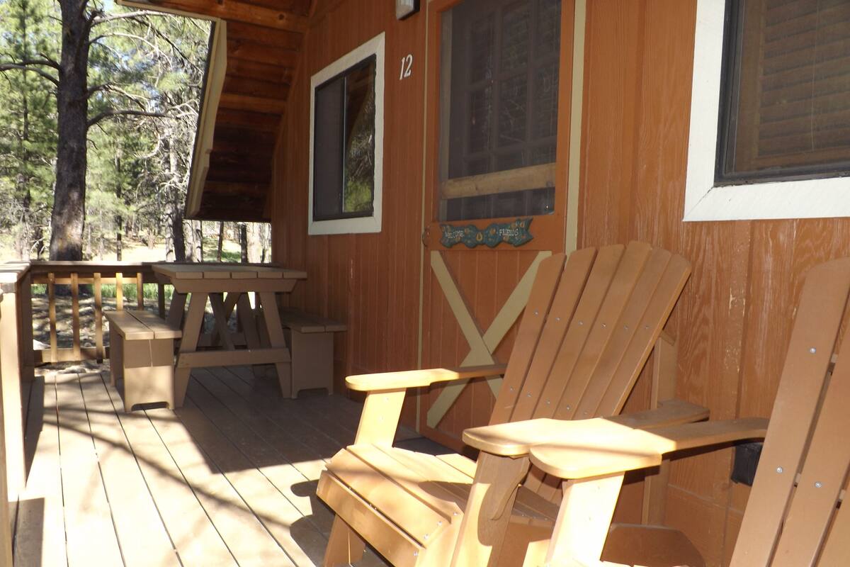 A wooden deck with two Adirondack chairs and a picnic table.