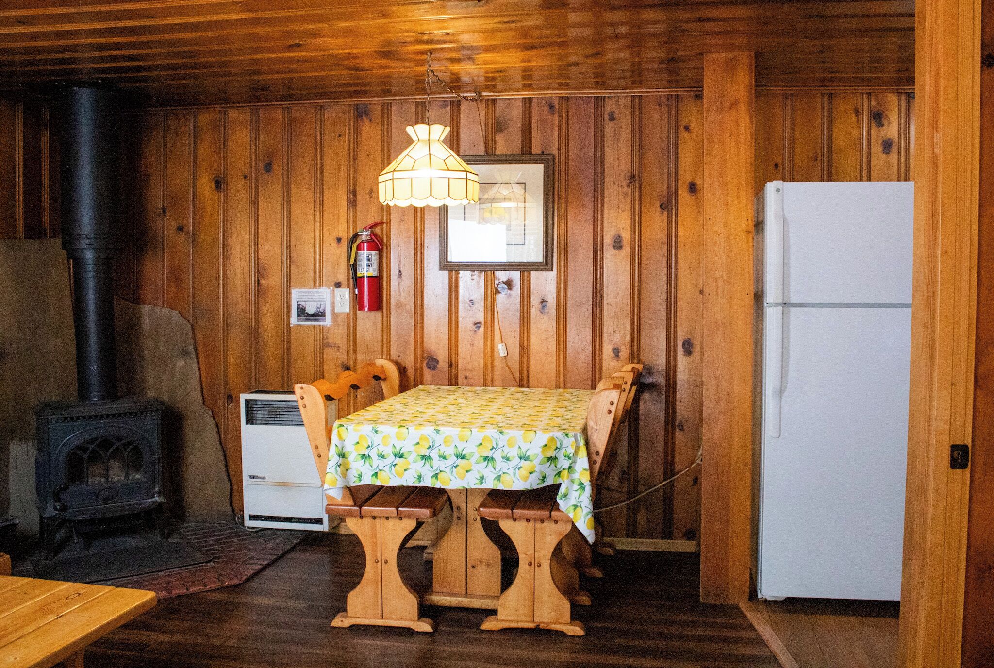 Un interior de madera con una mesa y sillas, un refrigerador blanco, una estufa y un extintor.