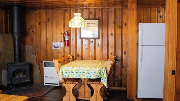 Un interior de madera con una mesa y sillas, un refrigerador blanco, una estufa y un extintor.
