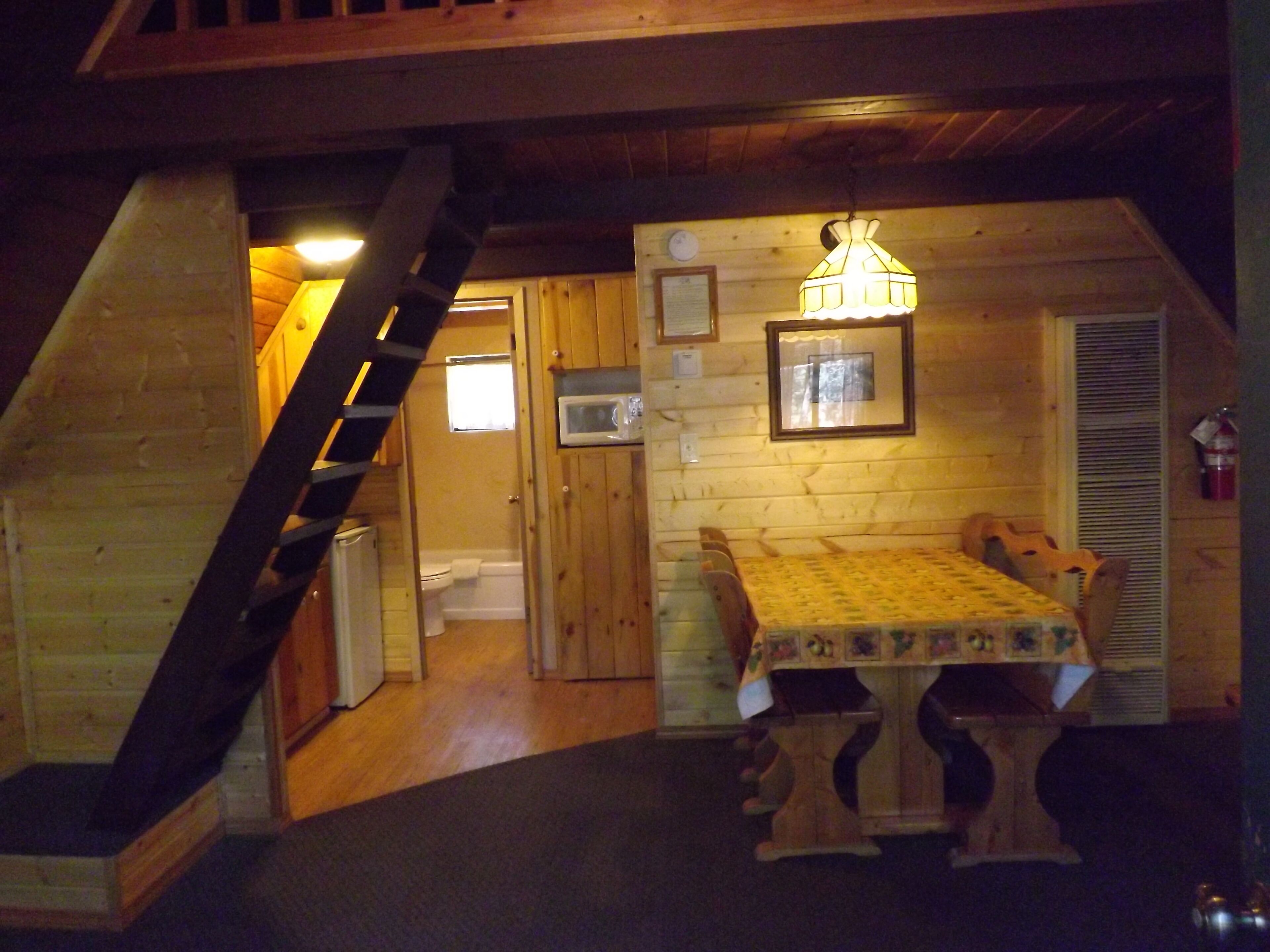 Accogliente baita in legno con tavolo da pranzo, una scala e un angolo cottura.