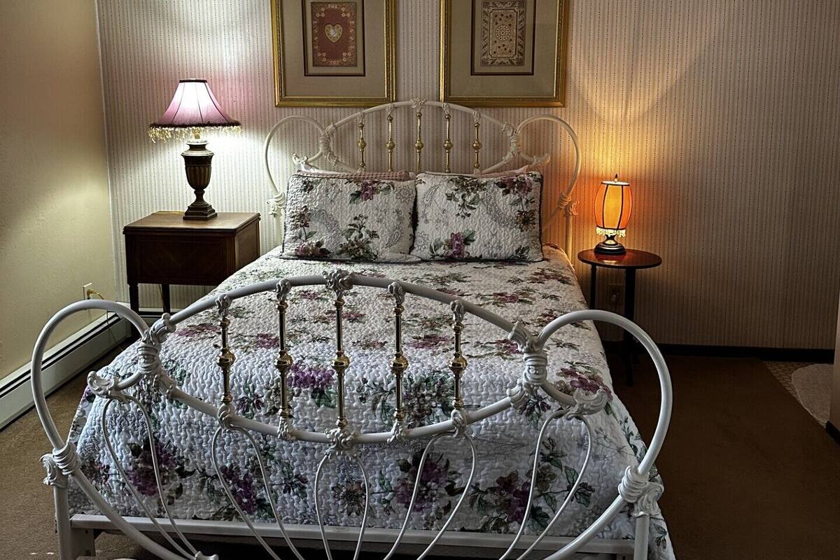 A bed with a floral bedspread and a metal frame, two framed pictures on the wall, and two bedside lamps.