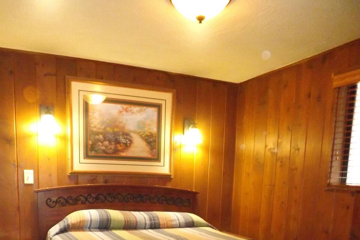 A wooden-paneled room with a bed, two wall sconces, and a framed picture above the bed.