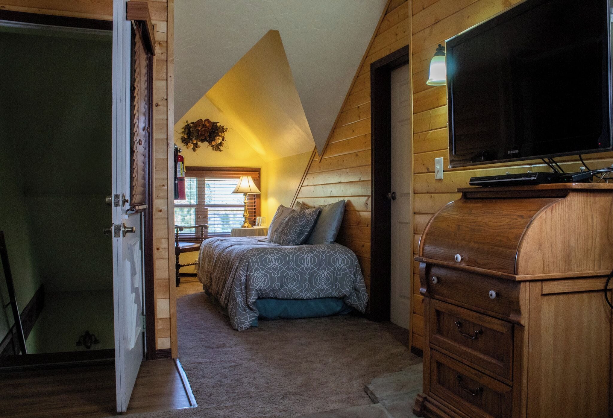 A bedroom with a bed, wooden walls, a television, and a dresser.