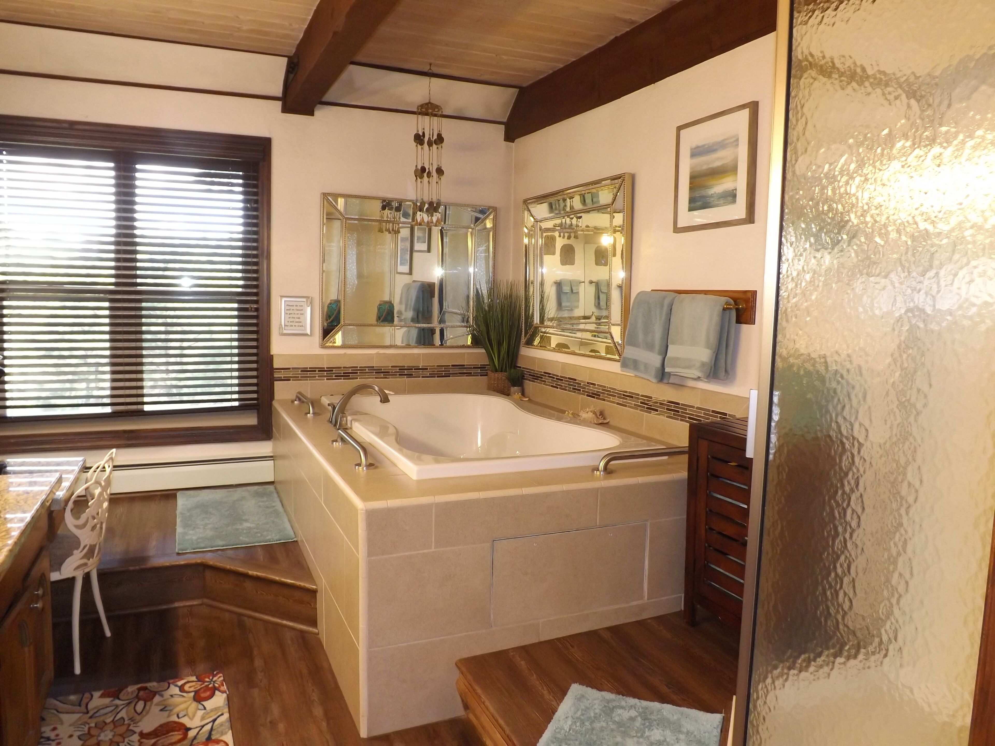 Ein Badezimmer mit einer großen Badewanne, einem Waschtisch mit Spiegel und einem Fenster mit Jalousien.