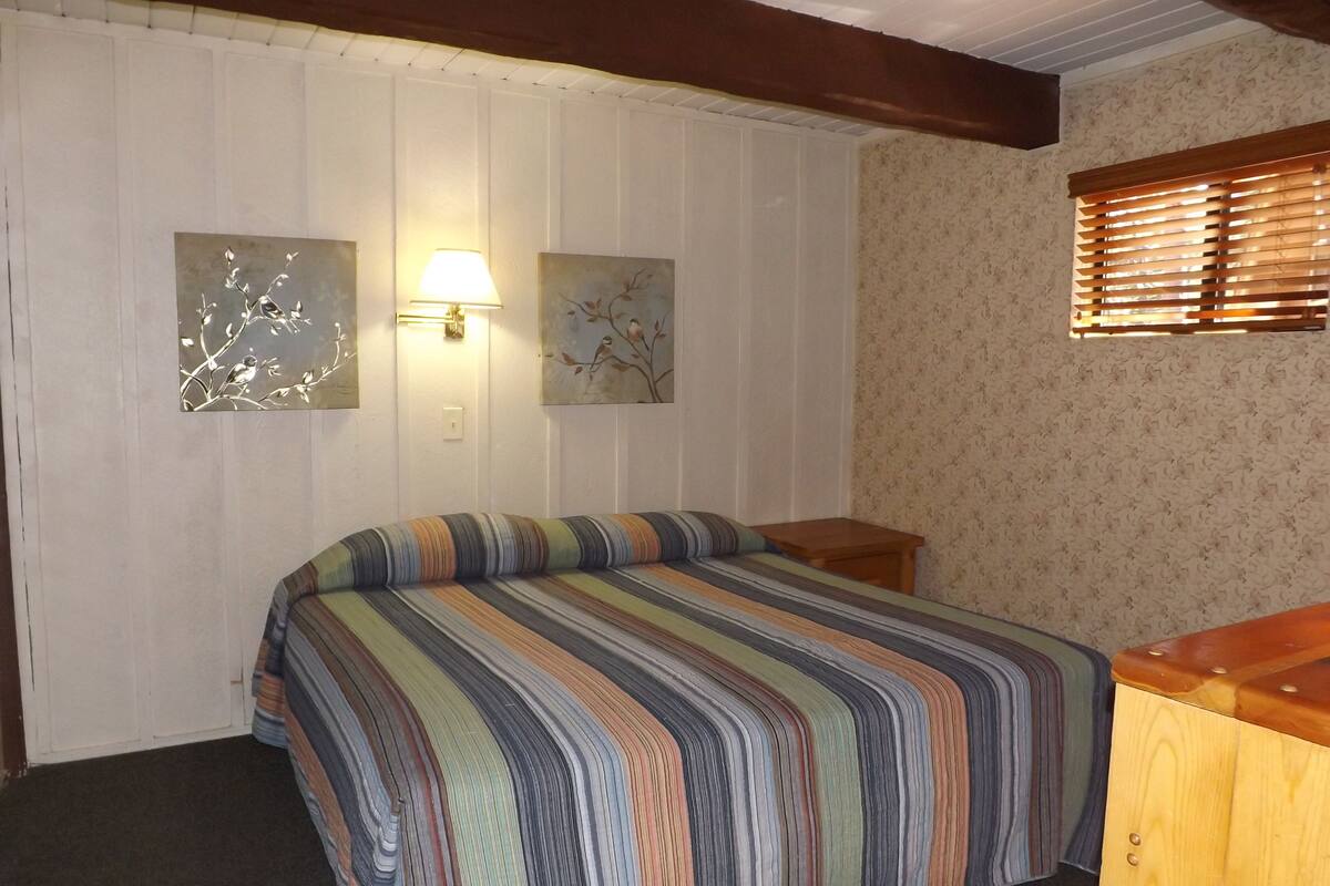 A bedroom with a bed, a nightstand, a lamp, and two wall-mounted artworks.