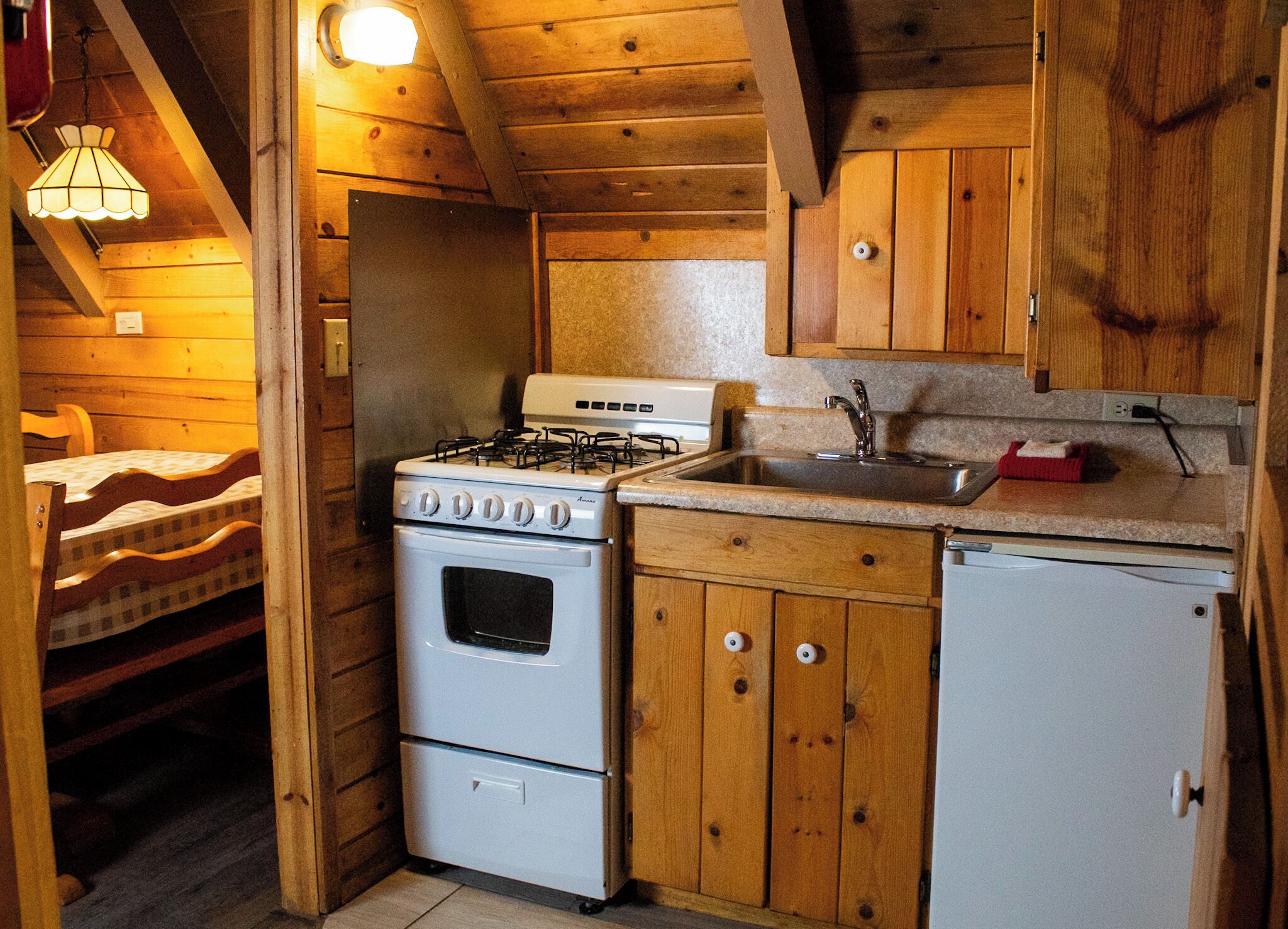 A compact kitchen with a stove, sink, and refrigerator, wooden cabinets, and a small dining area with a table and chairs.