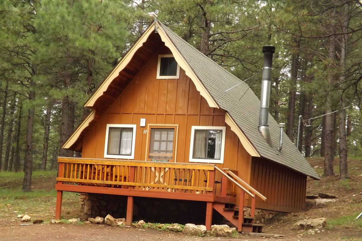 A wooden cabin with a porch, two windows, and a chimney.