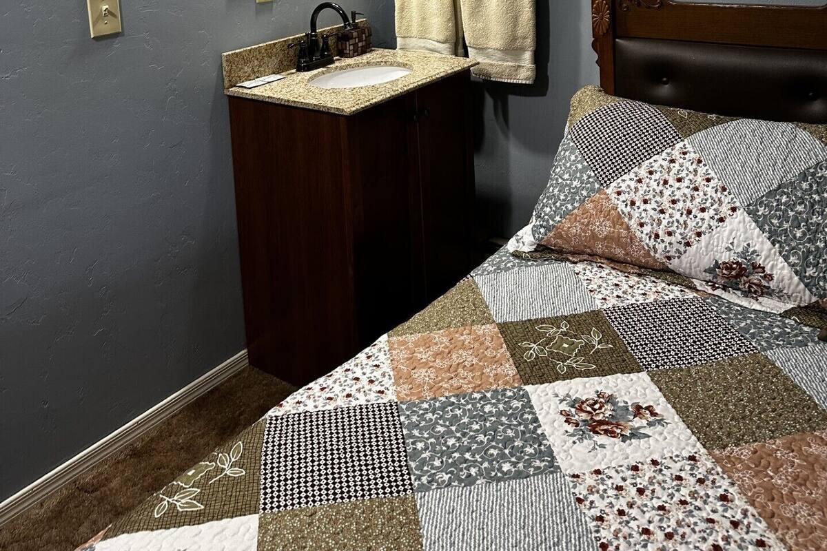 A bedroom with a wooden headboard, a bed with a patchwork quilt, a nightstand with a lamp, a mirror, and two towels hanging on hooks.