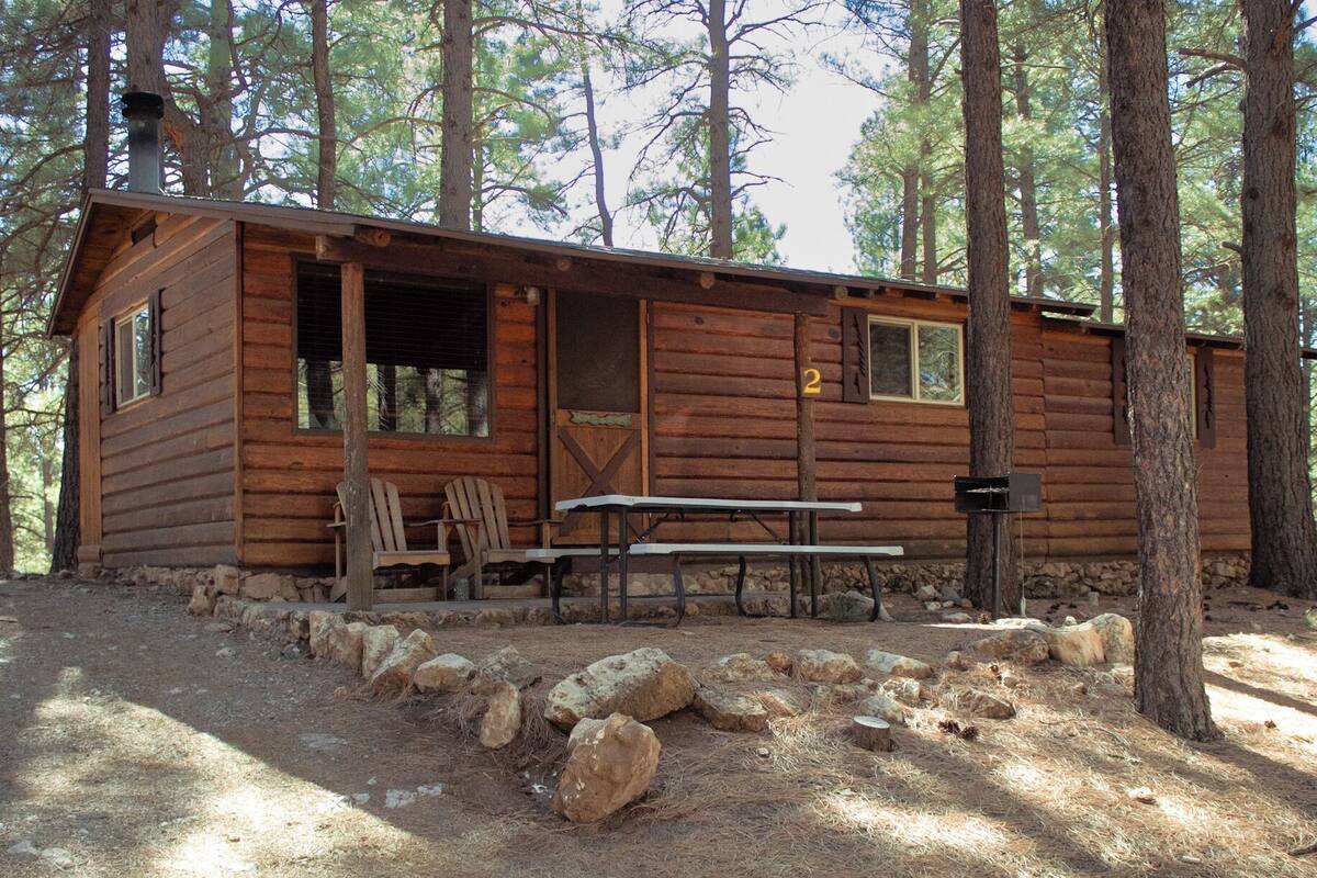 A rustic cabin with a porch, two chairs, and a table.