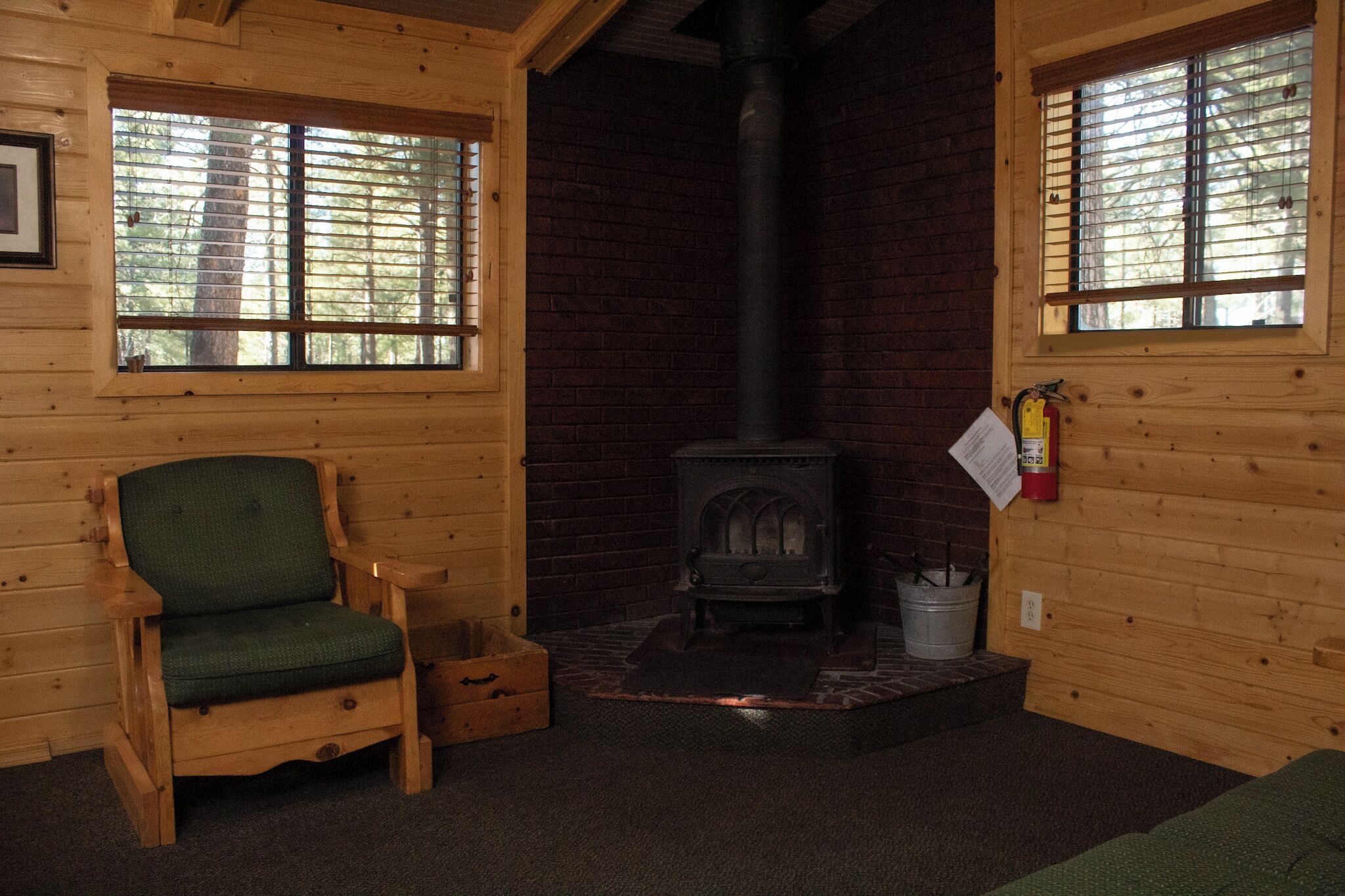 A cozy cabin interior with a wooden chair, a fireplace, and two windows.