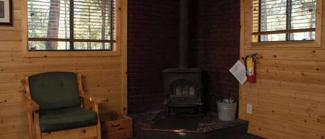 A cozy cabin interior with a wooden chair, a fireplace, and two windows.