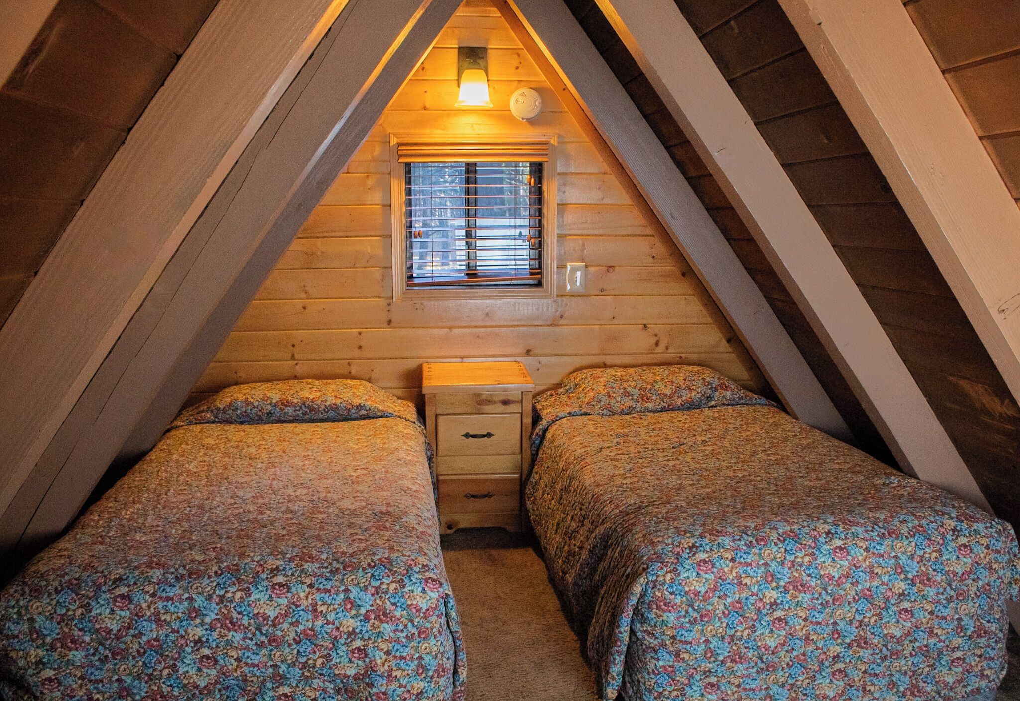 Un dormitorio acogedor en el ático, con dos camas, una ventana y una mesita de noche.