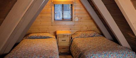 A small, cozy attic bedroom with two beds, a window, and a nightstand.