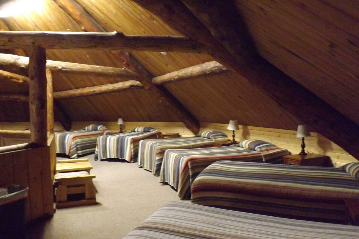A series of beds in a wooden attic room with sloped ceilings and exposed beams.