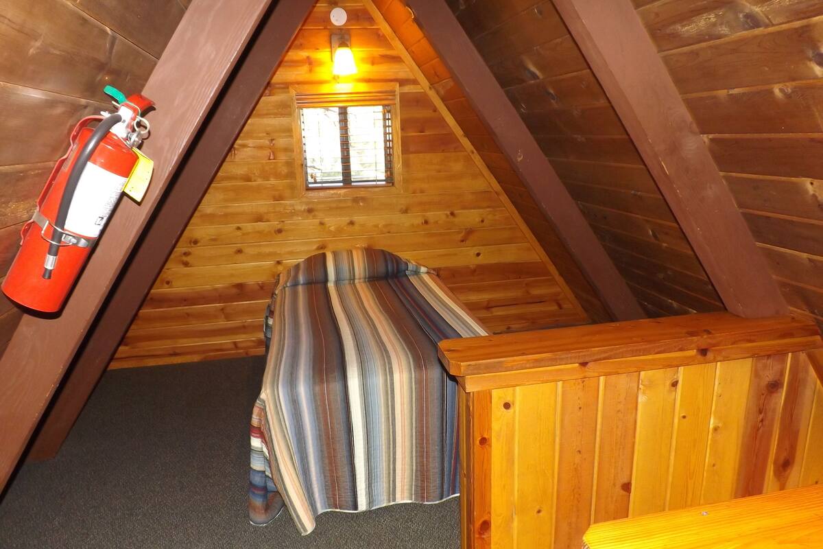 A small, cozy attic bedroom with a single bed, a window, and a fire extinguisher mounted on the wall.