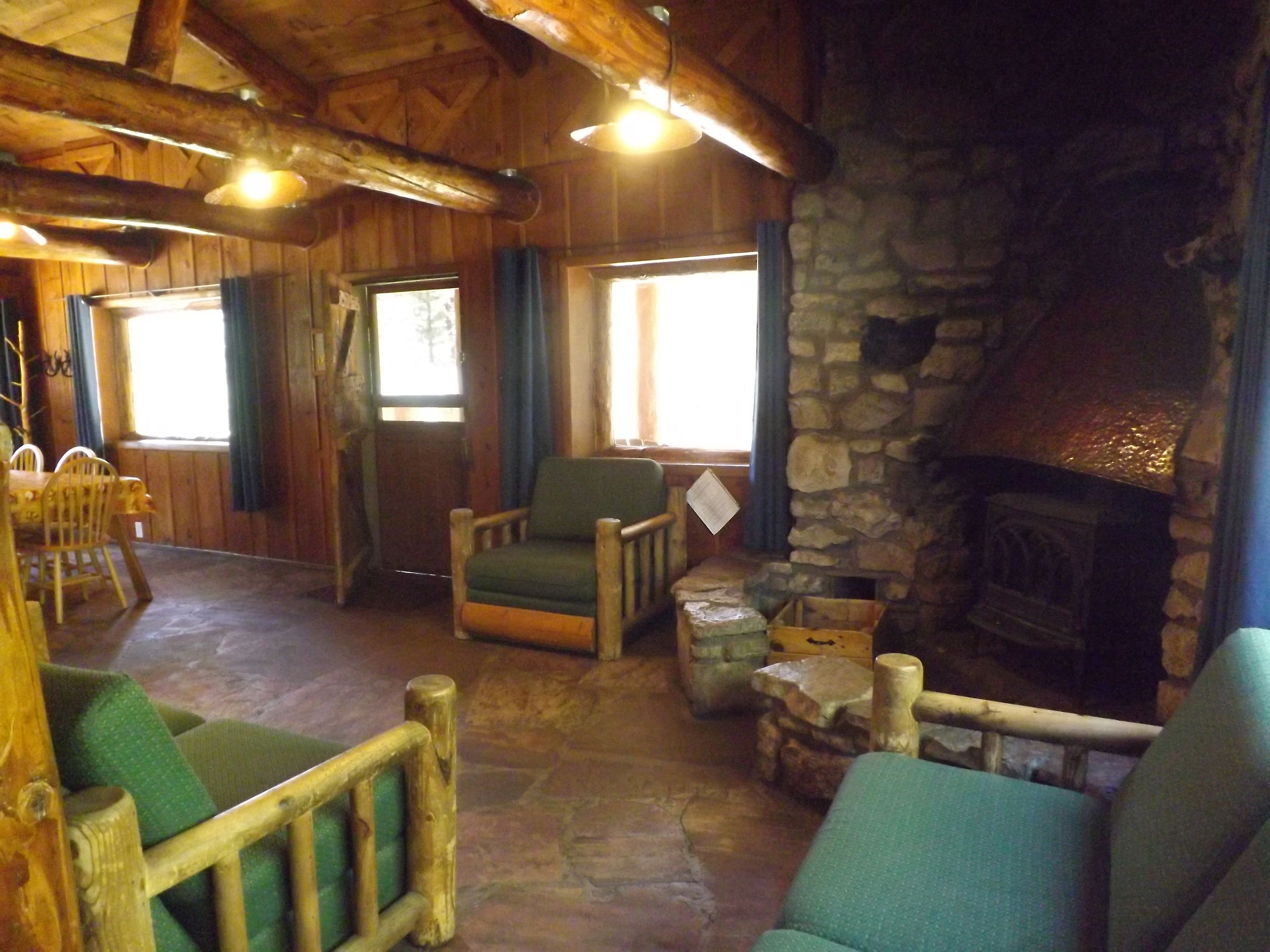A rustic interior with a stone fireplace, wooden furniture, and large windows allowing natural light.