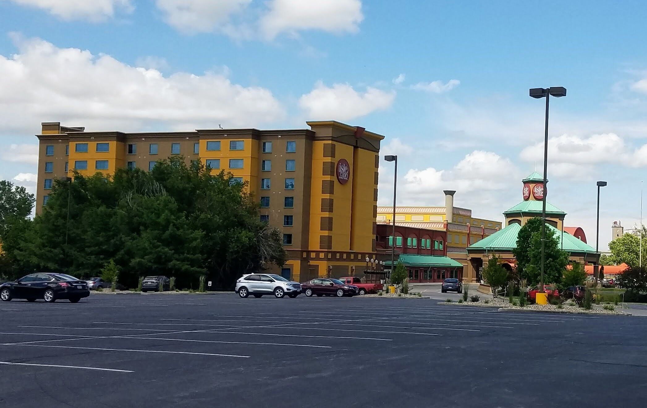 A hotel with multiple floors, a parking lot, and a small park area with trees.