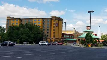 A hotel with multiple floors, a parking lot, and a small park area with trees.