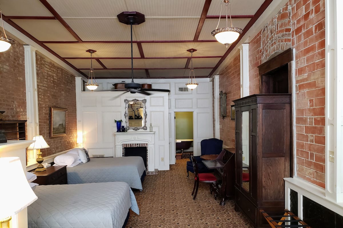 Ett hotellrum med två sängar, ett skrivbord, en stol, en öppen spis och en stor spegel.