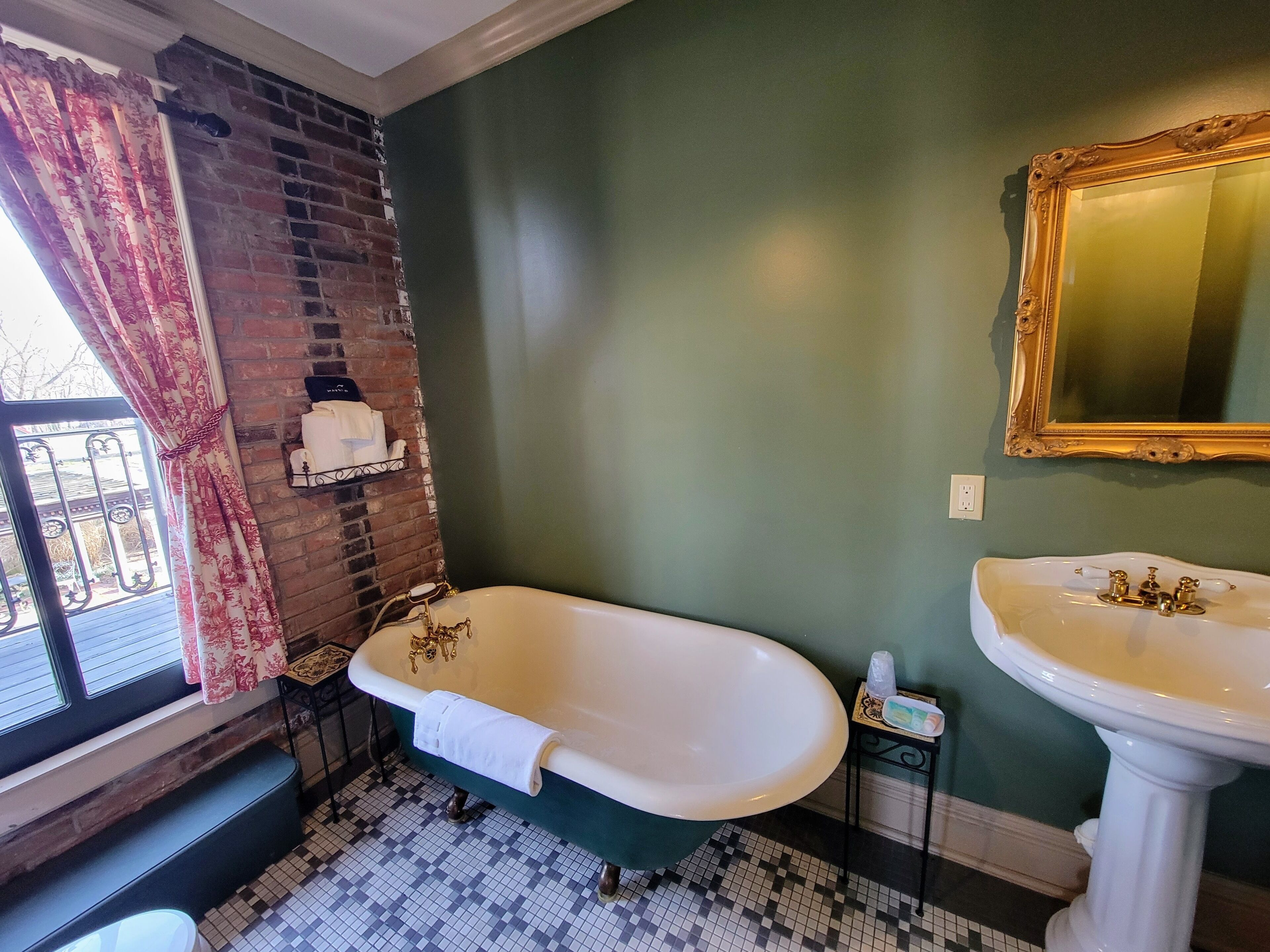 A bathroom with a freestanding bathtub, a pedestal sink, a mirror, and a window with curtains.