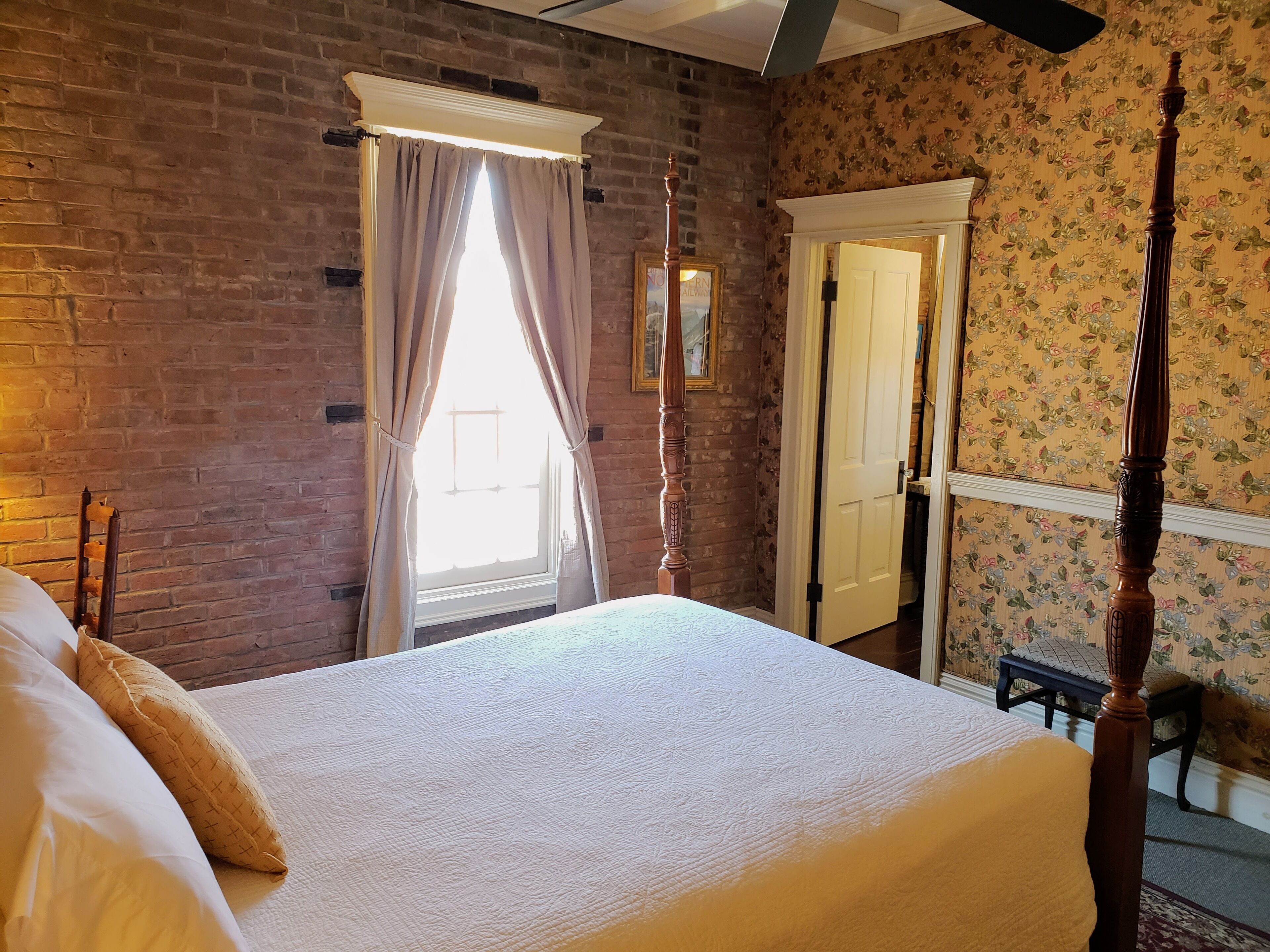 Un dormitorio con una cama grande, una ventana con cortinas, un cabecero de madera y una puerta con papel tapiz floral.