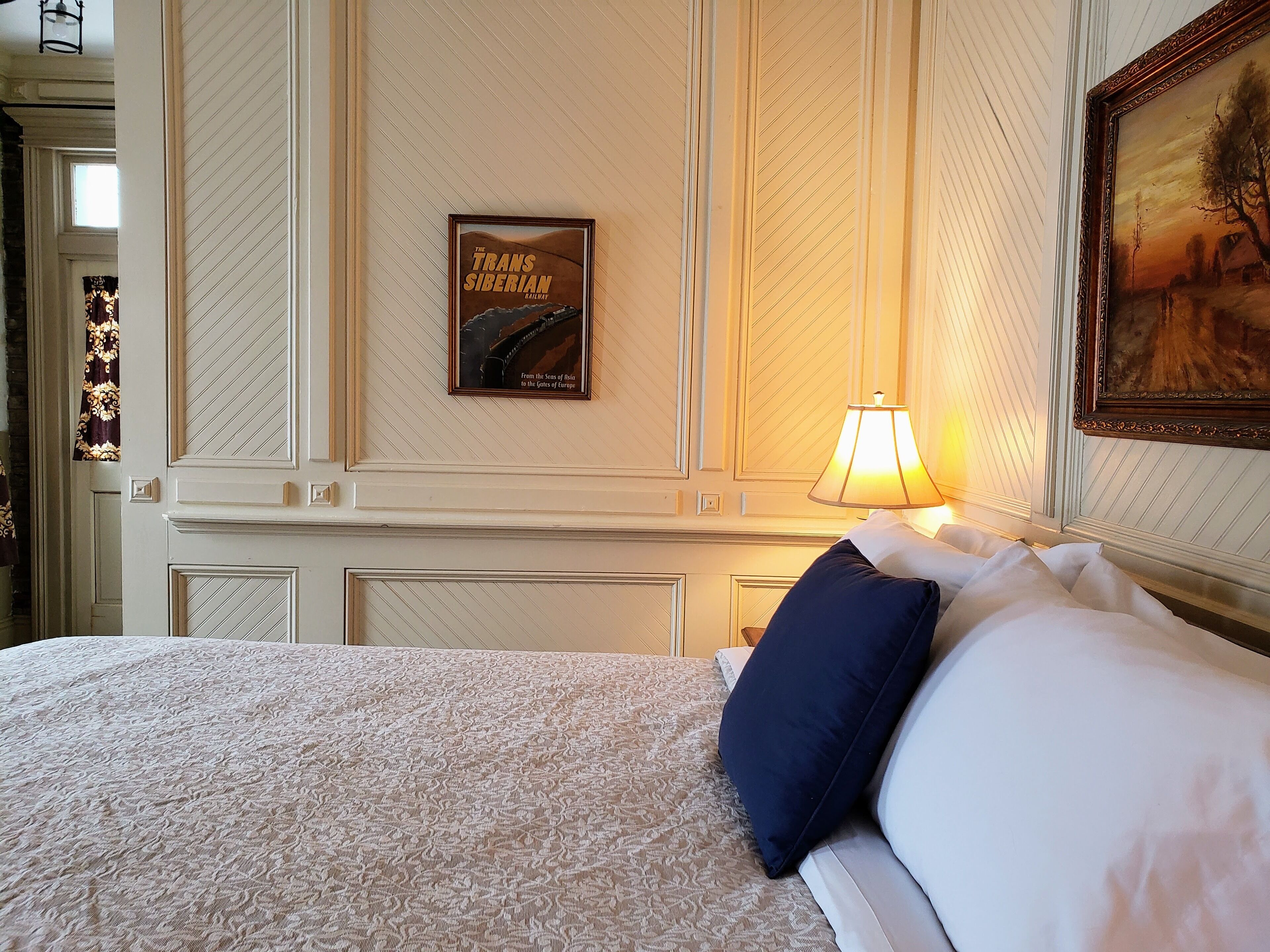 A hotel room with a bed, a framed picture of the Trans Siberian Railway, and a lamp.