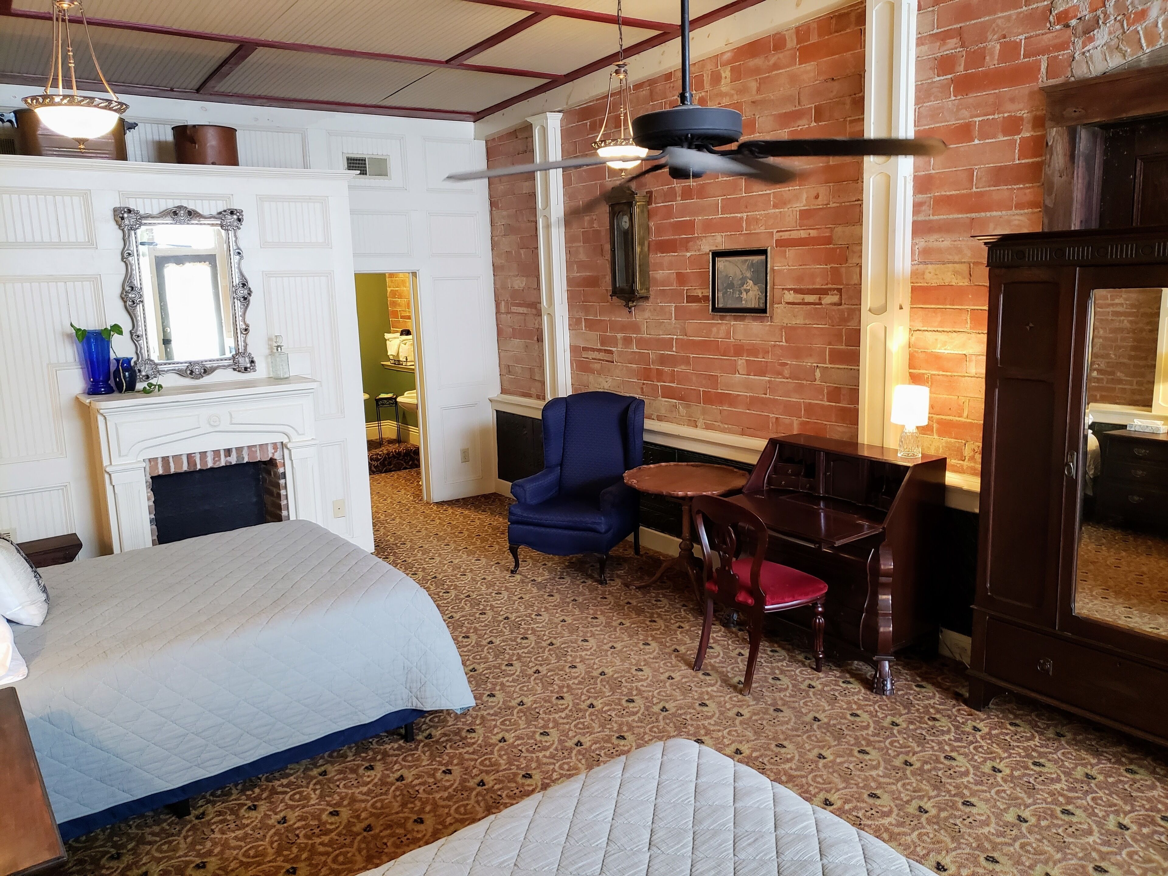 Una habitación de hotel con una cama, un sillón azul, una mesa de madera, una chimenea y una pared de ladrillo.