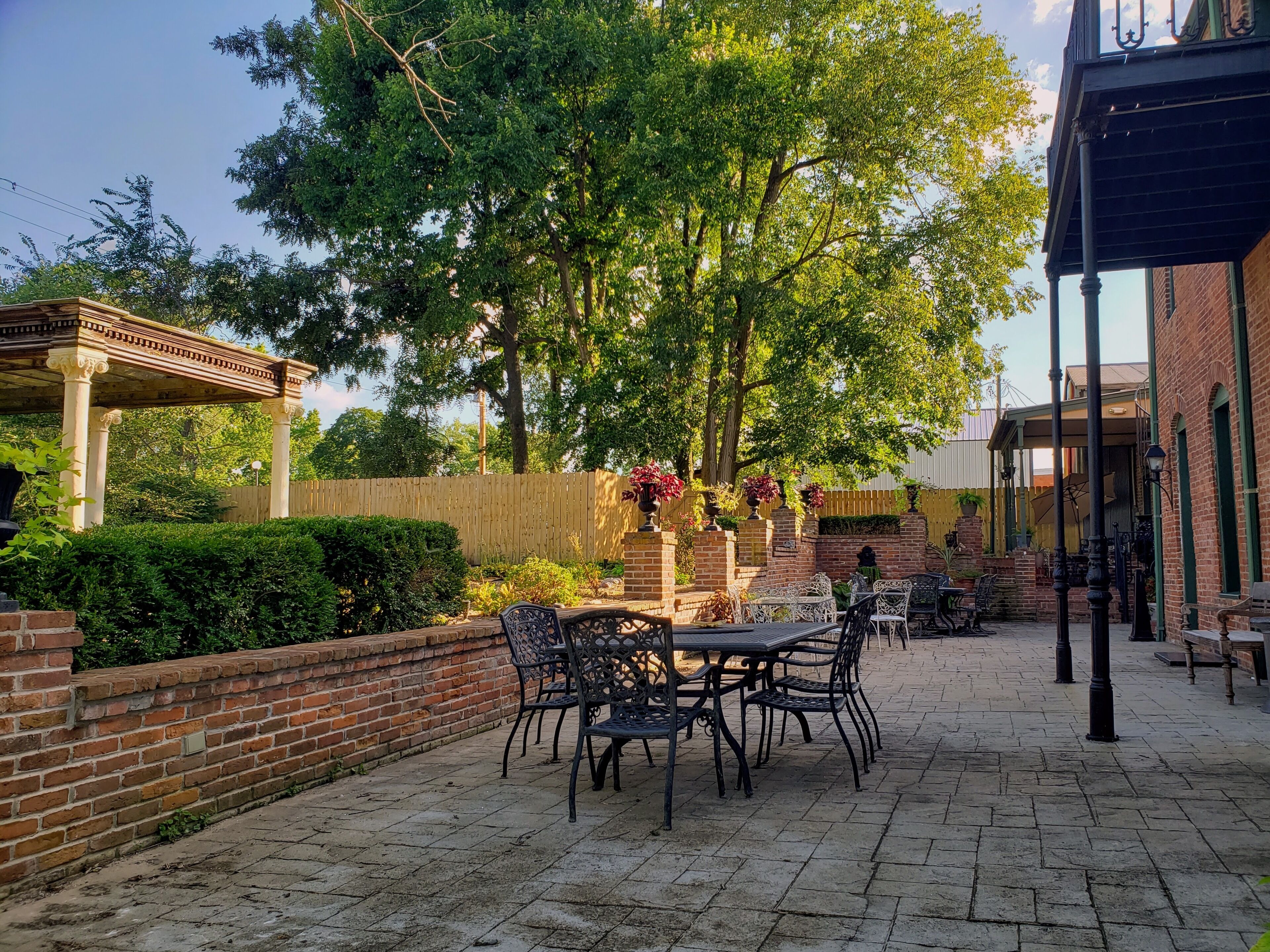Un patio con muro de ladrillo, pérgola y mobiliario exterior.