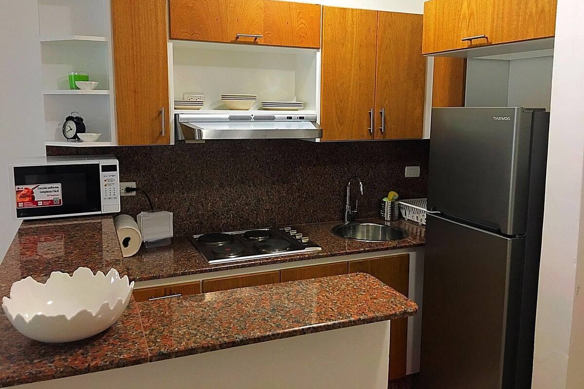 Una cocina compacta con armarios de madera, un refrigerador de acero inoxidable, un microondas, una estufa y un lavamanos.