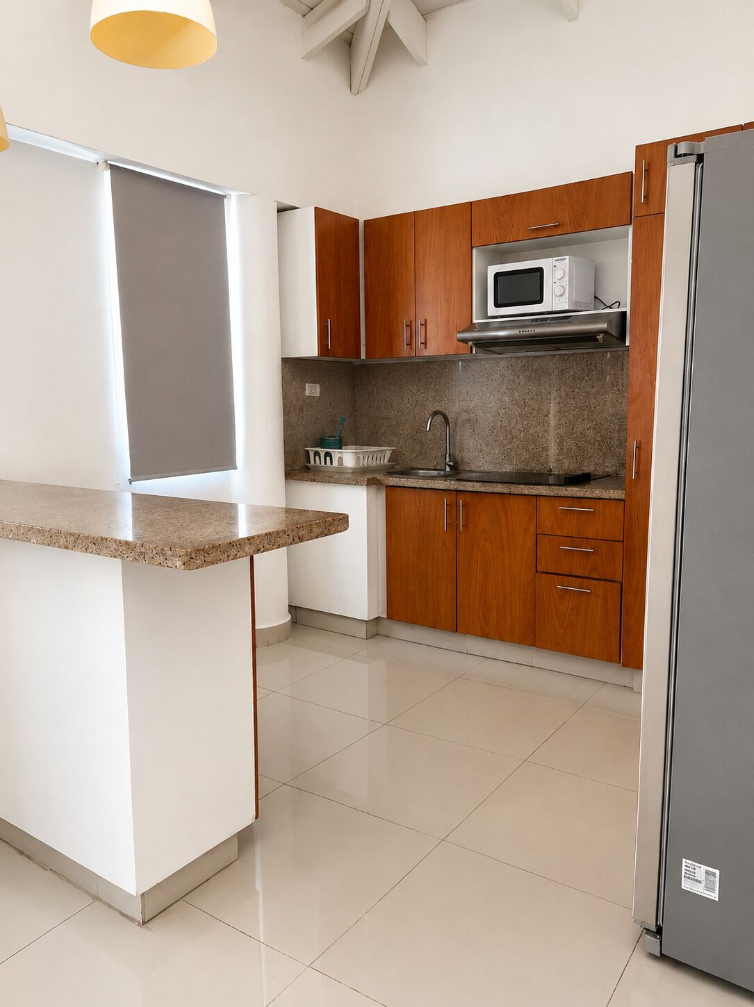A kitchen with a granite countertop, wooden cabinets, a stainless steel refrigerator, and a microwave.