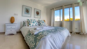 Une chambre à coucher avec un grand lit, des tables de chevet blanches et une fenêtre avec des rideaux.