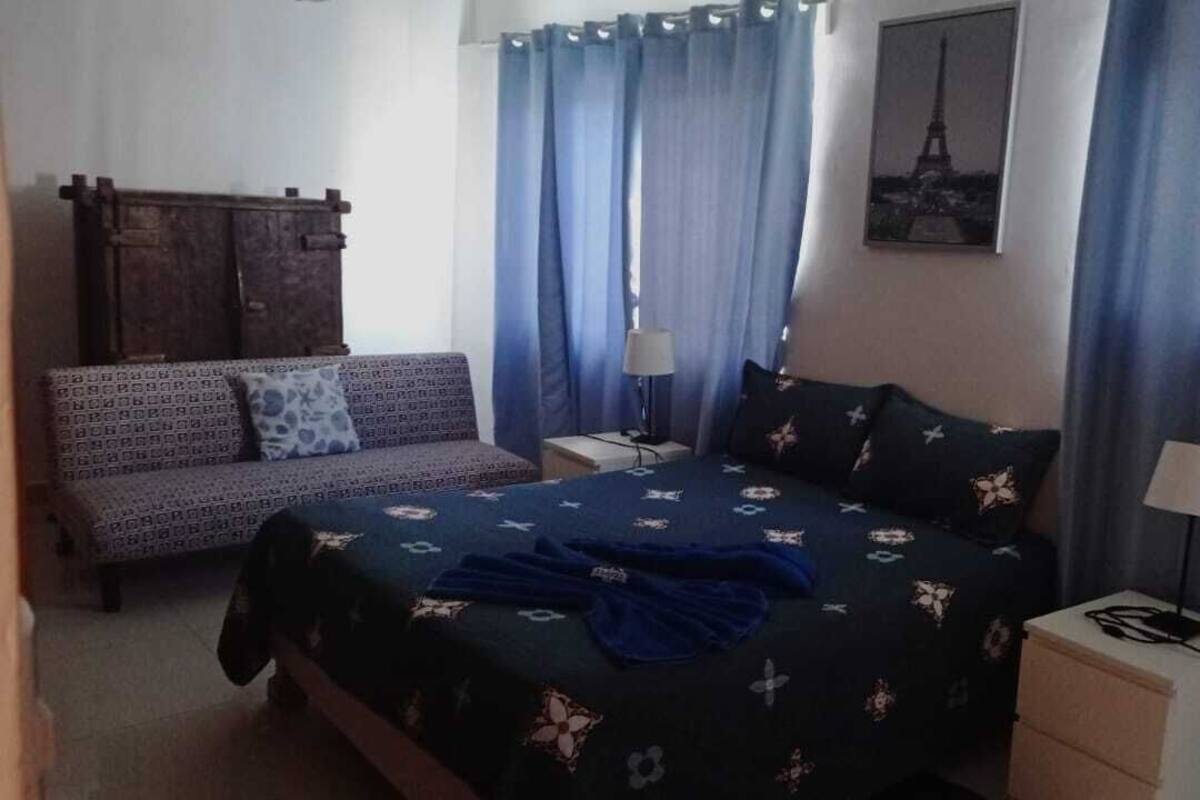 Un dormitorio con cama, sofá, dos mesitas de noche y cortinas.