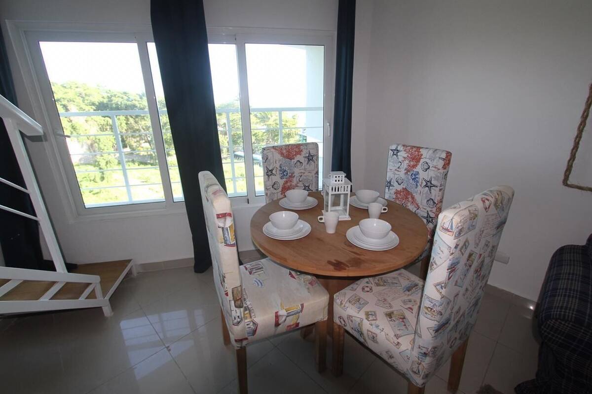 Un comedor con una mesa redonda de madera dispuesta con platos y tazas blancos, rodeada de sillas estampadas.