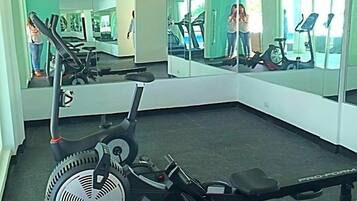 Un gimnasio con equipo de cardio, incluyendo una máquina elíptica y una bicicleta estática, y un espejo grande que refleja el espacio.