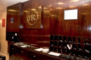 Un mostrador de recepción con detalles de madera, un cartel grande que dice 'RR.HH.', una vitrina de vidrio con objetos y un pequeño certificado enmarcado en la pared.