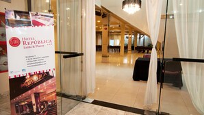 A hotel lobby with a glass partition, a reception desk, and a staircase leading to the upper floor. - Hotel República (San Miguel de Tucuman)