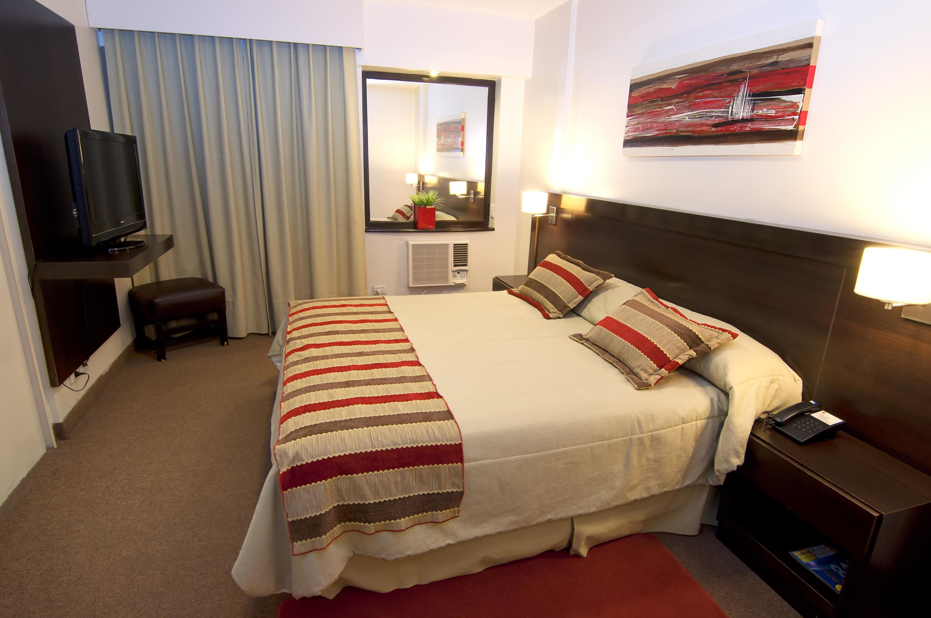 A hotel room with a large bed, a TV, a mirror, and a painting on the wall.
