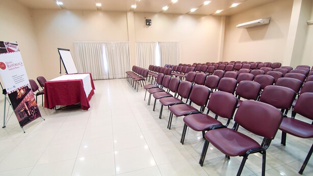 A conference room with rows of chairs, a table with a red tablecloth, a whiteboard, and a banner. - Hotel República (San Miguel de Tucuman)