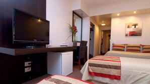 A hotel room with a flat-screen TV, a small fridge, a desk with a chair, a bed with striped bedding, and a painting on the wall. - Hotel República (San Miguel de Tucuman)