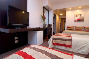 Habitación de hotel con televisión de pantalla plana, un refrigerador pequeño, un escritorio con silla, cama con ropa de cama a rayas y un cuadro en la pared.
