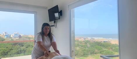 Una habitación con sesión de masajes, ventanas amplias y vista a un paisaje costero.