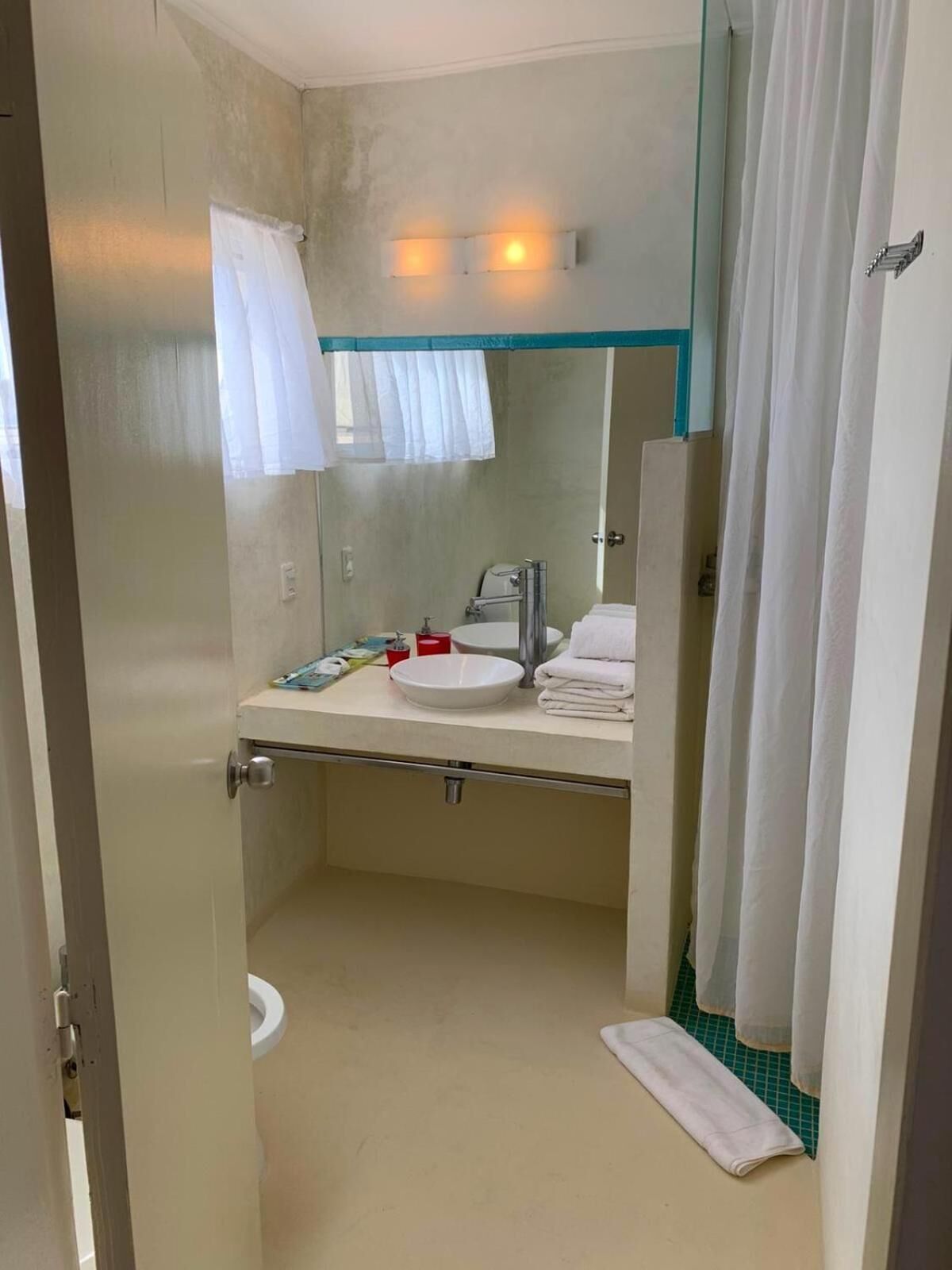 Un baño pequeño con un lavamanos blanco, un espejo y una cortina de ducha.