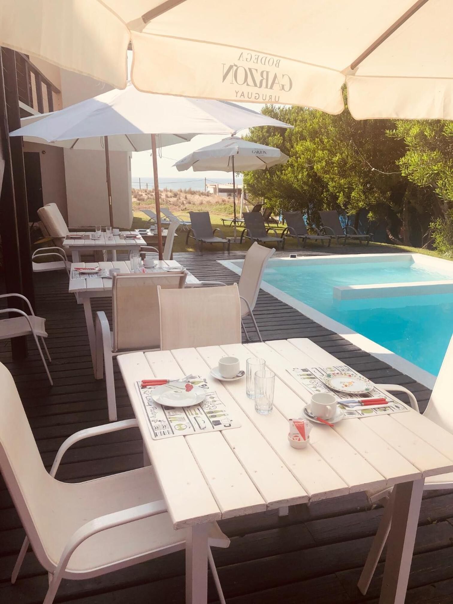 Un espace piscine extérieur avec des tables et des chaises blanches, des parasols et une vue sur le paysage.