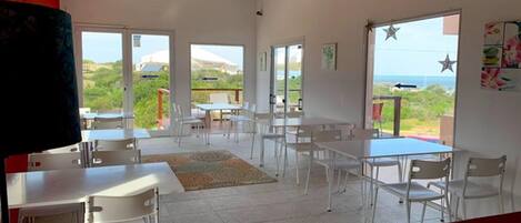 Una habitación amplia con mobiliario blanco, ventanas grandes y vistas al exterior.