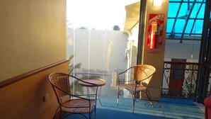Een hotel lobby met rieten stoelen en een tafeltje, een blauw tapijt en uitzicht op buiten.