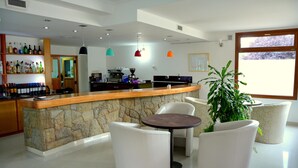 A modern bar area with a stone counter, white seating, and a large window. - Cumbres Hotel (El Bolson)
