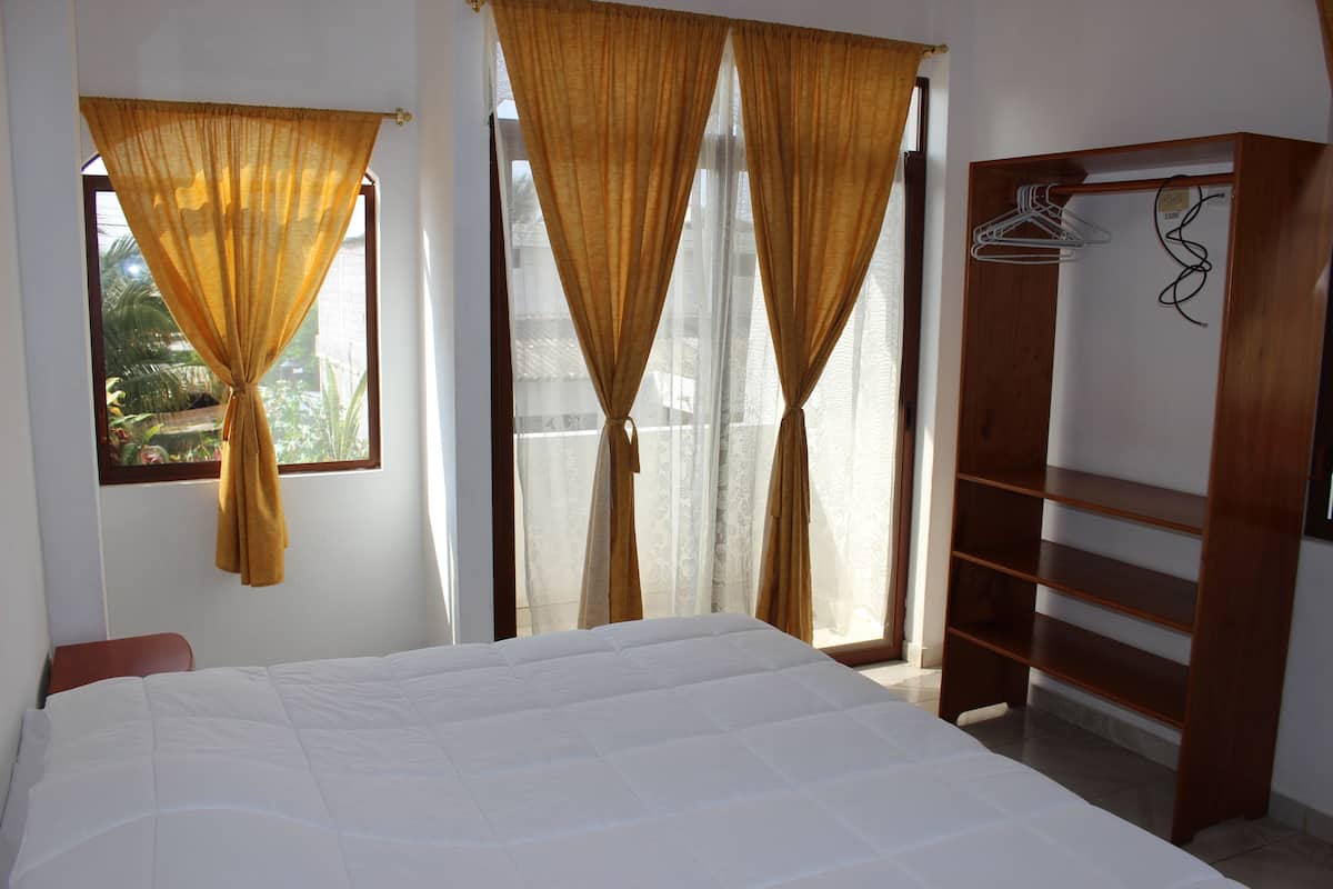A bedroom with a bed, curtains, a wardrobe, and a window with a view.